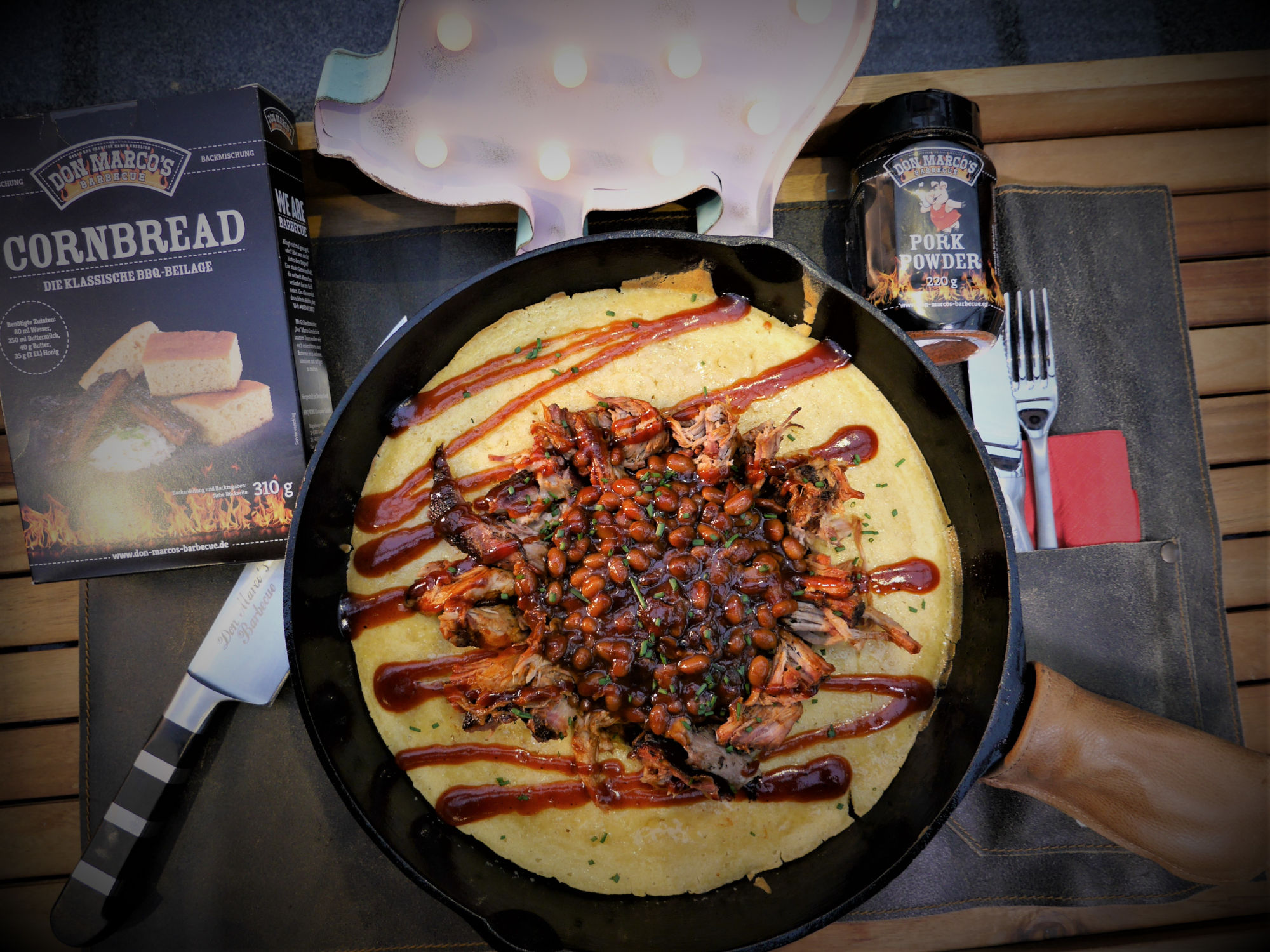 Pulled Pork auf Cornbread garniert mit BBQ Sauce in Gußpfanne auf Lederschürze